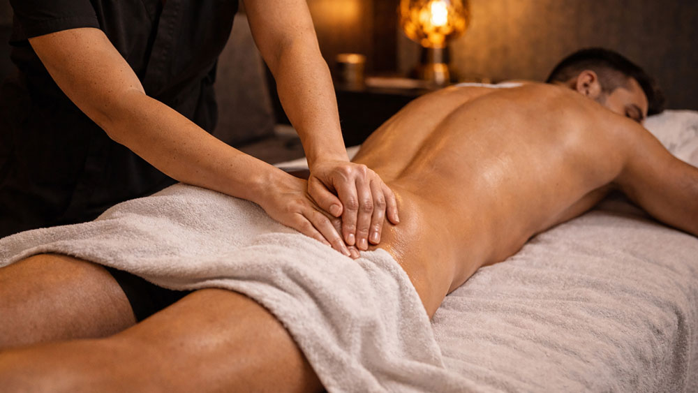 Lower back cross fiber sports massage Belgrade hotel room, female therapist applying horizontal friction across male client muscles